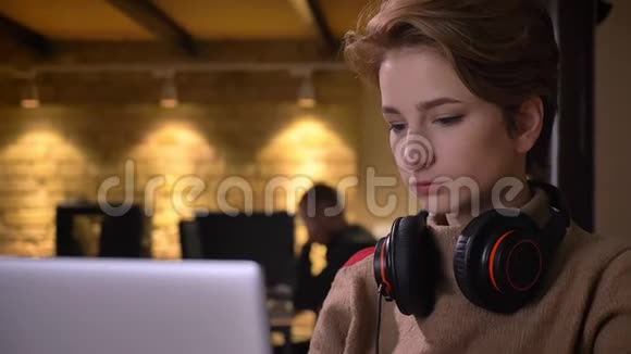 一位留着耳机手提电脑和饮料的短发年轻女性的特写镜头视频的预览图