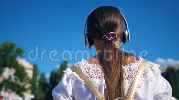 穿着白色连衣裙留着长发的少女在蓝天的映衬下环游城市慢动作一个年轻女孩走着视频的预览图