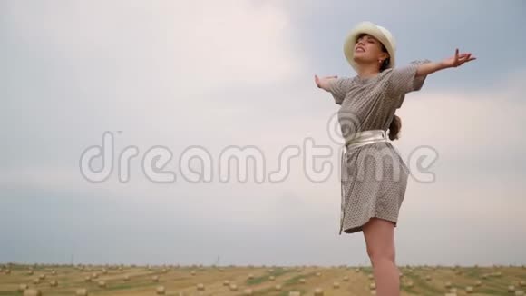 戴着帽子的漂亮年轻女子望着天空双手举到麦田中央的天空上挂着捆视频的预览图