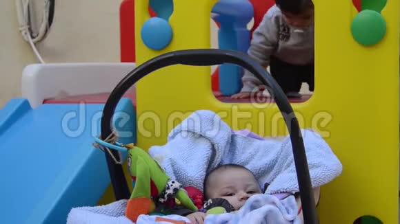 大树几个月大的小男孩在婴儿床上玩耍而他的哥哥则在塑料玩具屋里玩滑梯视频的预览图