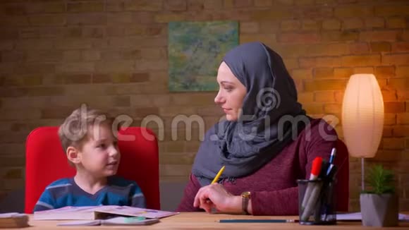 在家中的餐桌上穆斯林母亲和她的小儿子在头巾学习信中近距离拍摄视频的预览图