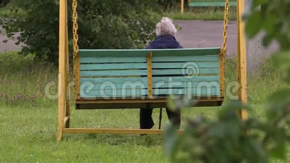 秋天和阴天一位老妇人坐在花园里荡秋千视频的预览图