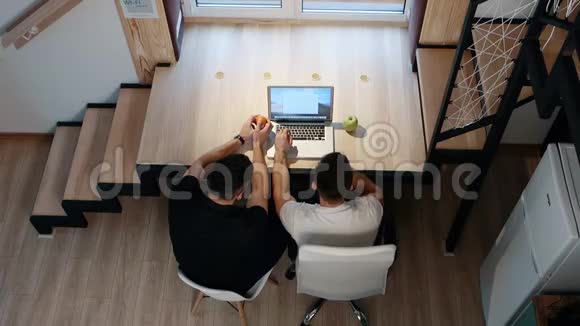 两名男性在笔记本电脑上工作坐在桌子旁家庭办公室的概念上景视频的预览图