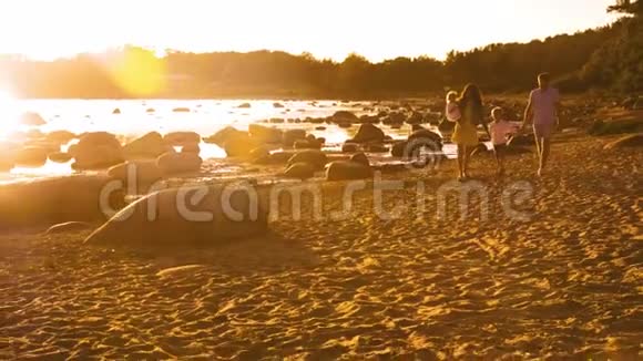 幸福的一家人走在海边海滩和海洋日落或日出的暖色可爱的父母和美丽的视频的预览图