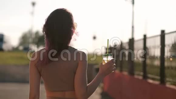 戴着太阳镜的年轻美女正在城市街道上用吸管从玻璃罐里喝鸡尾酒视频的预览图