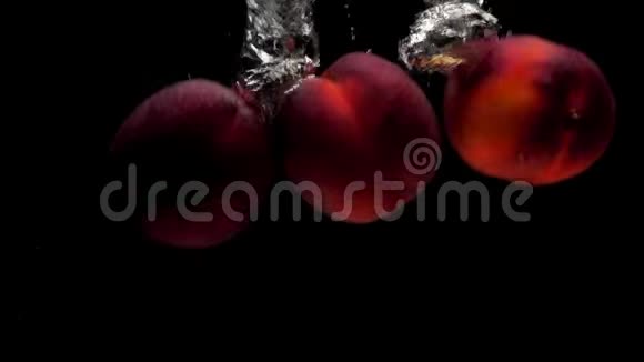 三个成熟的桃子在黑色的背景下落入透明的水中视频的预览图