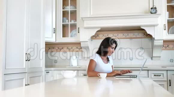 微笑自由职业者妇女工作写文字使用笔记本电脑老式家庭厨房视频的预览图