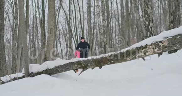 一男一女冬天在公园里跑跳过一棵倒下的树跨过障碍视频的预览图