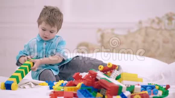 小男孩在卧室的床上和设计师玩男孩和一个多色设计师玩幸福的概念视频的预览图