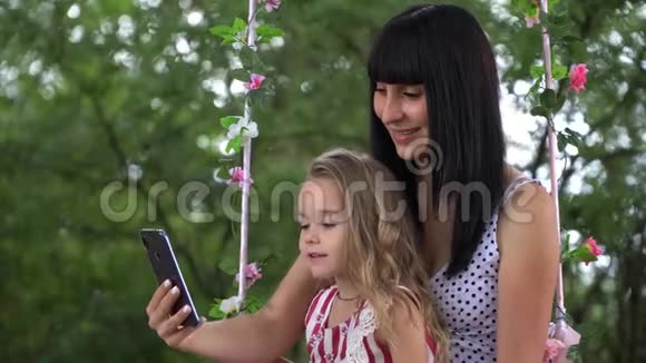 美丽的年轻母女笑着看着大自然中的电话视频的预览图