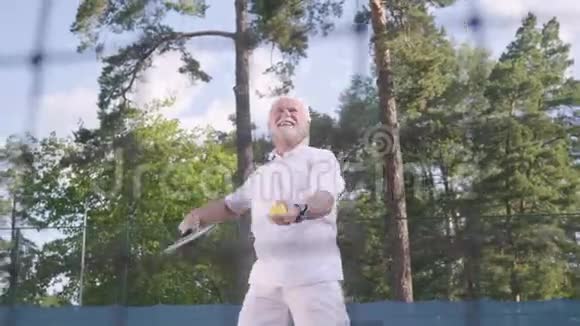 积极微笑的成熟男人在网球场上打网球老人用球拍扔球积极主动视频的预览图