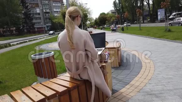 坐在长凳上用笔记本电脑工作的女孩视频的预览图