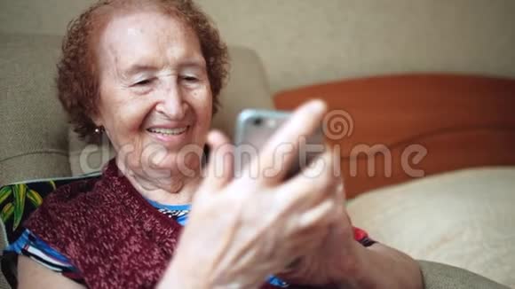 一位老妇人写了一条信息看着她新智能手机上的照片奶奶的皱纹很深印支快乐视频的预览图