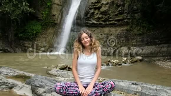 女人坐在莲花的位置在一个大瀑布的背景上做练习视频的预览图
