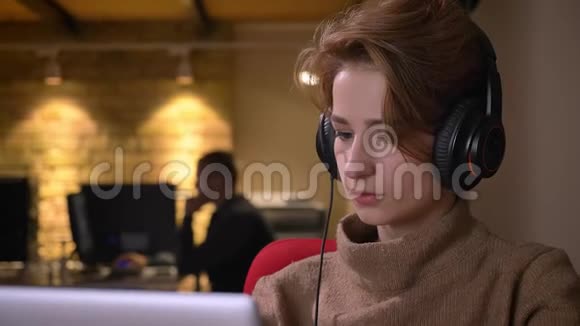 年轻的短发女士戴着耳机专心地用笔记本电脑和饮料在里面工作视频的预览图