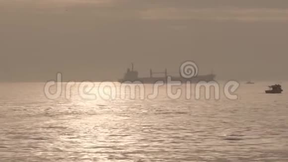 一艘大货轮矗立在阳光照耀下的大海上小船漂浮在海面上视频的预览图