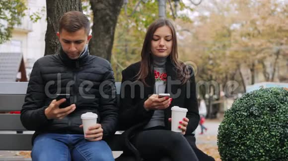 朋友们上网一边喝咖啡一边在街上坐在长凳上聊天视频的预览图