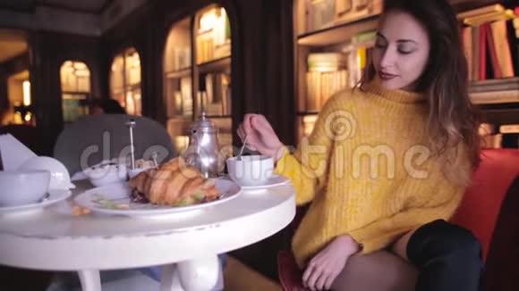 穿着黄色毛衣的年轻美女在舒适的咖啡馆里吃早餐喝茶视频的预览图