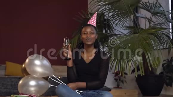 戴着香槟酒杯和气球的非洲年轻女子坐在地上拿着红色的相机视频的预览图