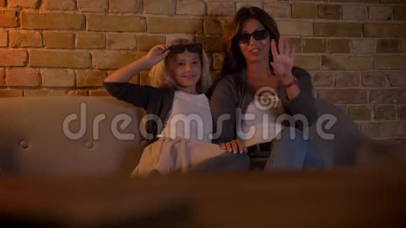 一位年轻的白种人女性和她的小女儿在家用3D眼镜看动作电影电视的特写镜头视频的预览图
