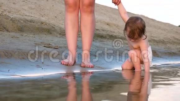 穿着尿布的快乐小男孩和妈妈在沙滩上散步孩子握着妈妈的手慢动作视频的预览图