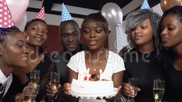 快乐迷人的年轻非洲女人在生日蛋糕上吹蜡烛包围了她的朋友视频的预览图