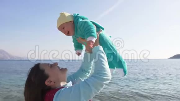 在阳光明媚的春天快乐的妈妈把她的孩子抱在沙滩上视频的预览图