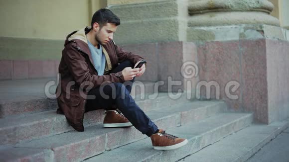有魅力的男人用电话坐在公园的台阶上视频的预览图