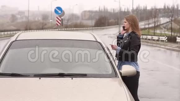 一个女孩在雨中在路上的一辆破车旁打电话视频的预览图