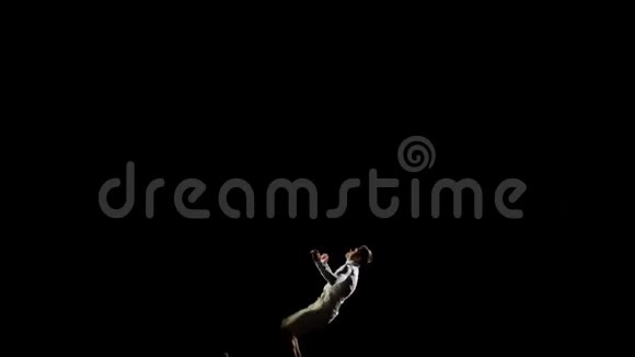一位英俊的白人男子体操运动员在黑色背景下做杂技特技动作缓慢旋转和翻转感觉有感觉视频的预览图