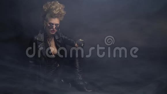 金发女人穿着皮制摇臂夹克和太阳镜摆弄着头发黑色的烟熏背景视频的预览图
