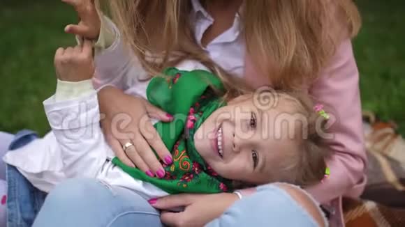 肖像一个微笑的小女孩躺在妈妈秋天公园的手上4k慢动作视频的预览图