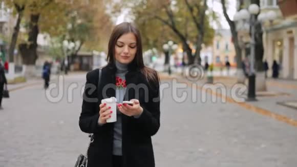 女人走在街上检查邮件看电话里的新闻喝咖啡视频的预览图