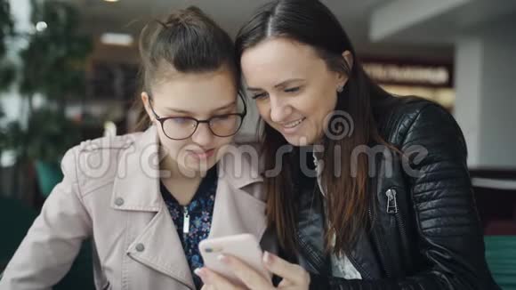 母女俩饶有兴致地看着智能手机里的照片坐在咖啡馆的一张桌子旁视频的预览图