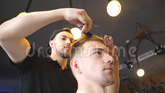 英俊的理发师在沙龙为他的客户修剪头发男理发师通过他的顾客梳理和理发视频的预览图