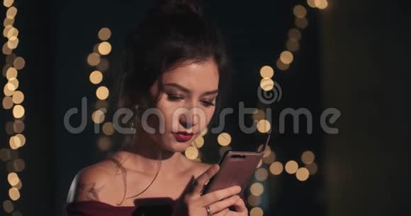 一个迷人的年轻女子的肖像她看着电话微笑新年圣诞节生日假期a视频的预览图