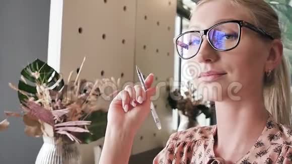 一位带眼镜的年轻女学生在咖啡馆的桌子上的肖像咖啡馆里的金发美女慢动作视频的预览图