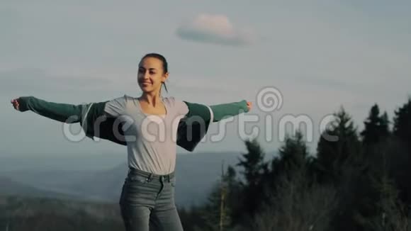 年轻的女徒步旅行者站在山岭边缘站在夕阳的背景下视频的预览图