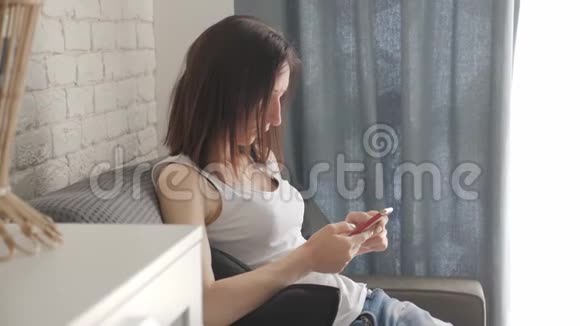 年轻女子躺在沙发上在智能手机上进行网上购物网上购物的概念视频的预览图