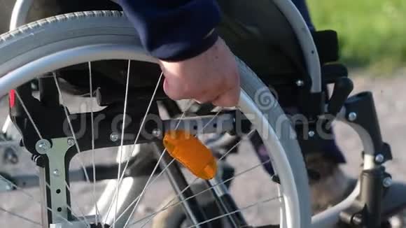 残疾人用双手转动轮椅车轮骑在土路上视频的预览图