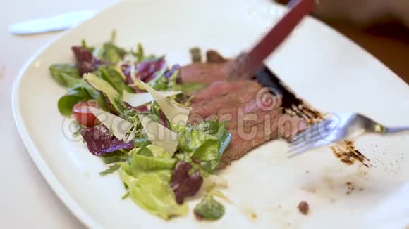 盘子里放着沙拉的肉片手用叉子和勺子轻轻地切下一小块肉视频的预览图