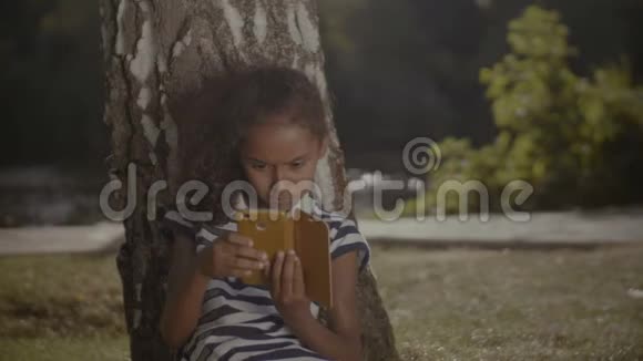 可爱的女孩在树下用手机联网视频的预览图