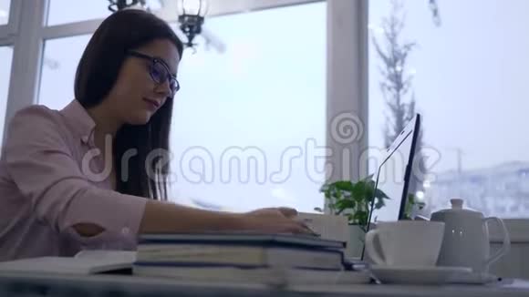 在网上学习学生女孩使用笔记本电脑并在笔记本上写笔记坐在咖啡馆的桌子上背景是大型的视频的预览图