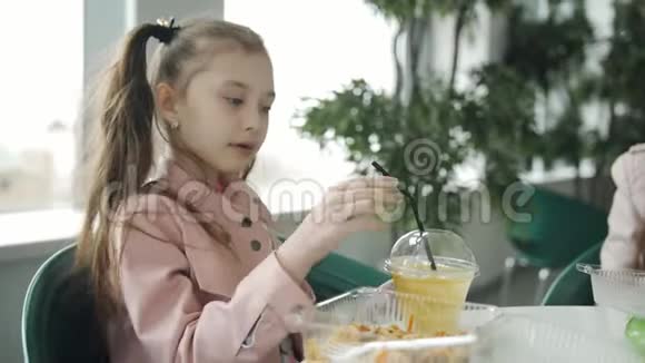 小女孩在咖啡馆里吃面条喝稻草上的胡萝卜汁女孩在一个塑料杯里喝果汁视频的预览图