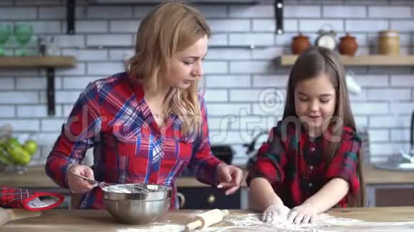 漂亮的年轻妈妈金发混在盘子里小可爱的淘气女孩在厨房里玩面粉视频的预览图