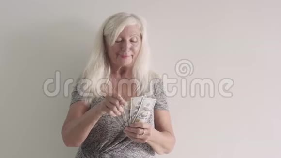 老妇人很高兴得到钱金发祖母微笑着展示她的收入一位拿着一捆钱的退休女士视频的预览图