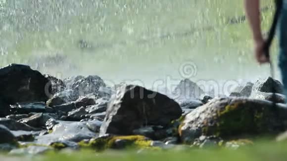 一个地下喷泉从地面上的岩石之间飞来前景上的一个人用棍子探地视频的预览图