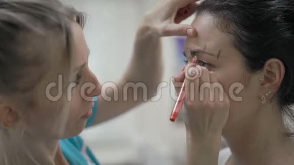特写美容师在一位美丽客户的眉毛周围标出红色轮廓视频的预览图