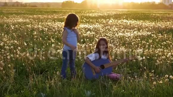 春日快乐两个有趣的迷人的小妹妹在草地上唱歌和弹声牛仔裤吉他女孩们玩得开心视频的预览图