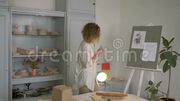 波特职业开朗的工匠女性绘制未来陶土的素描在桌子上滚动陶土的同时跳舞视频的预览图